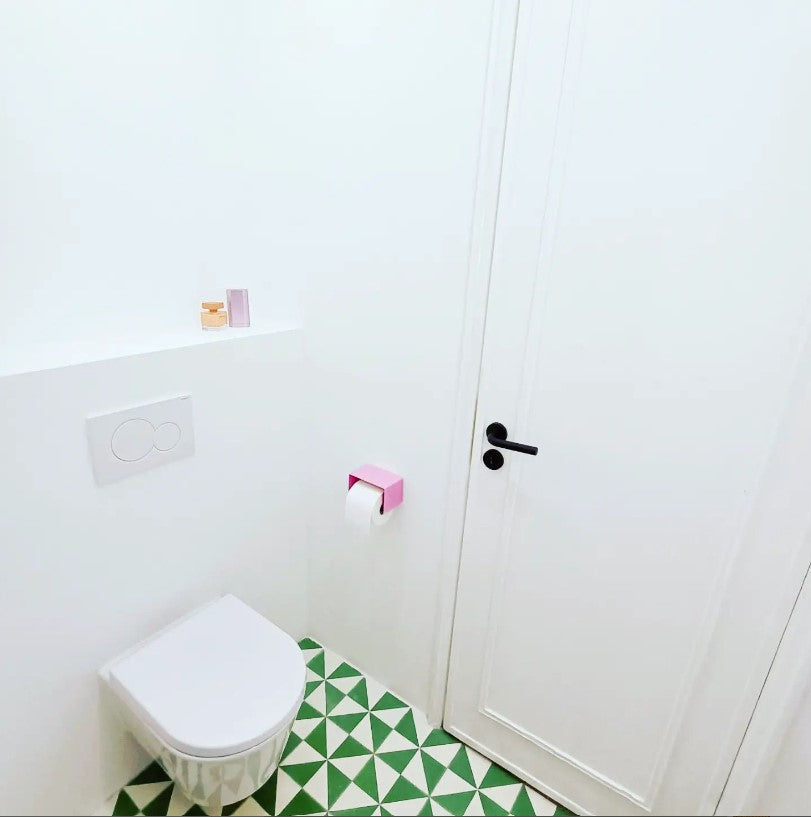 pink toilet paper holder in nice design where you can put things on top like a phone or candle or some small accessories.  Here shown in an actual bathroom with green tiles