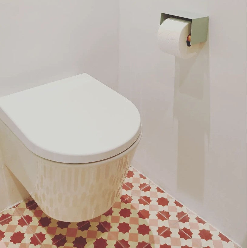 sage green toilet paper holder in nice design where you can put things on top like a phone or candle or some small accessories.  Here displayed in actual bathroom