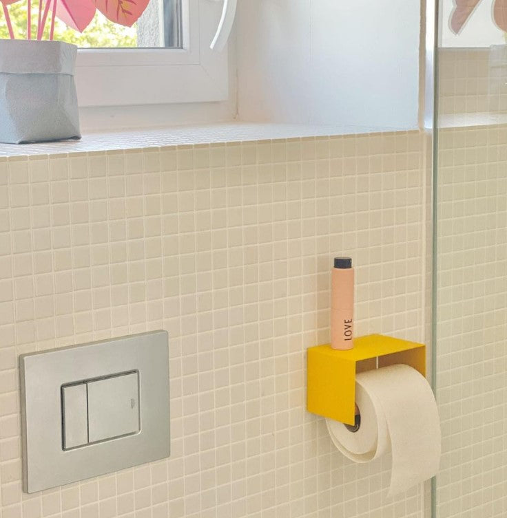 yellow toilet paper holder in nice design where you can put things on top like a phone or some small accessories. Here shown in an actual bathroom