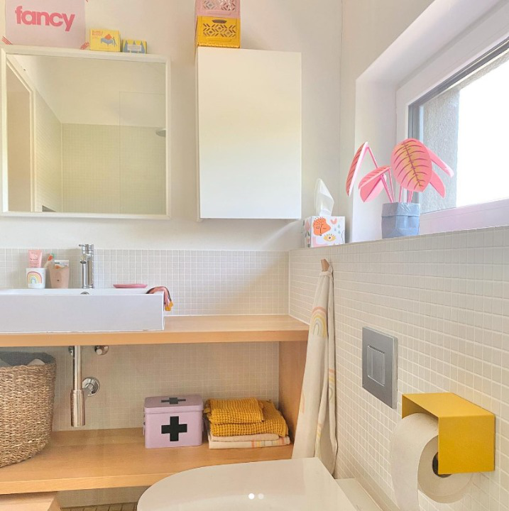 yellow toilet paper holder in nice design where you can put things on top like a phone or some small accessories. Here shown in an actual bathroom